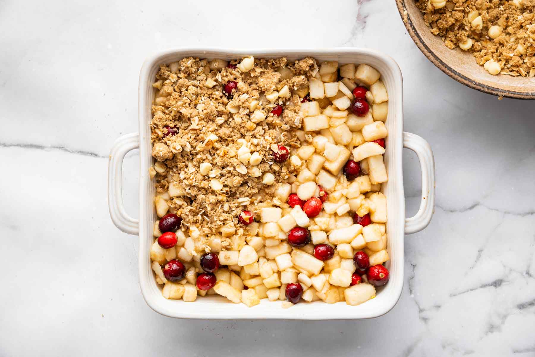 Square baking dish with chopped fruit, cranberries, and oat streusel on top.