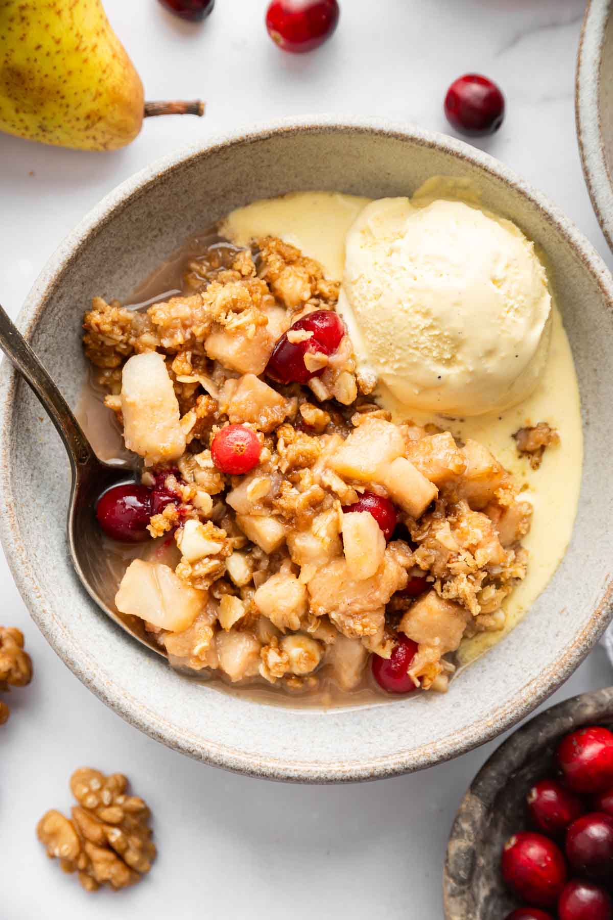 DessertForTwoPearCranberryCrisp3 Pear cobbler in a bowl with melted ice cream on the side.
