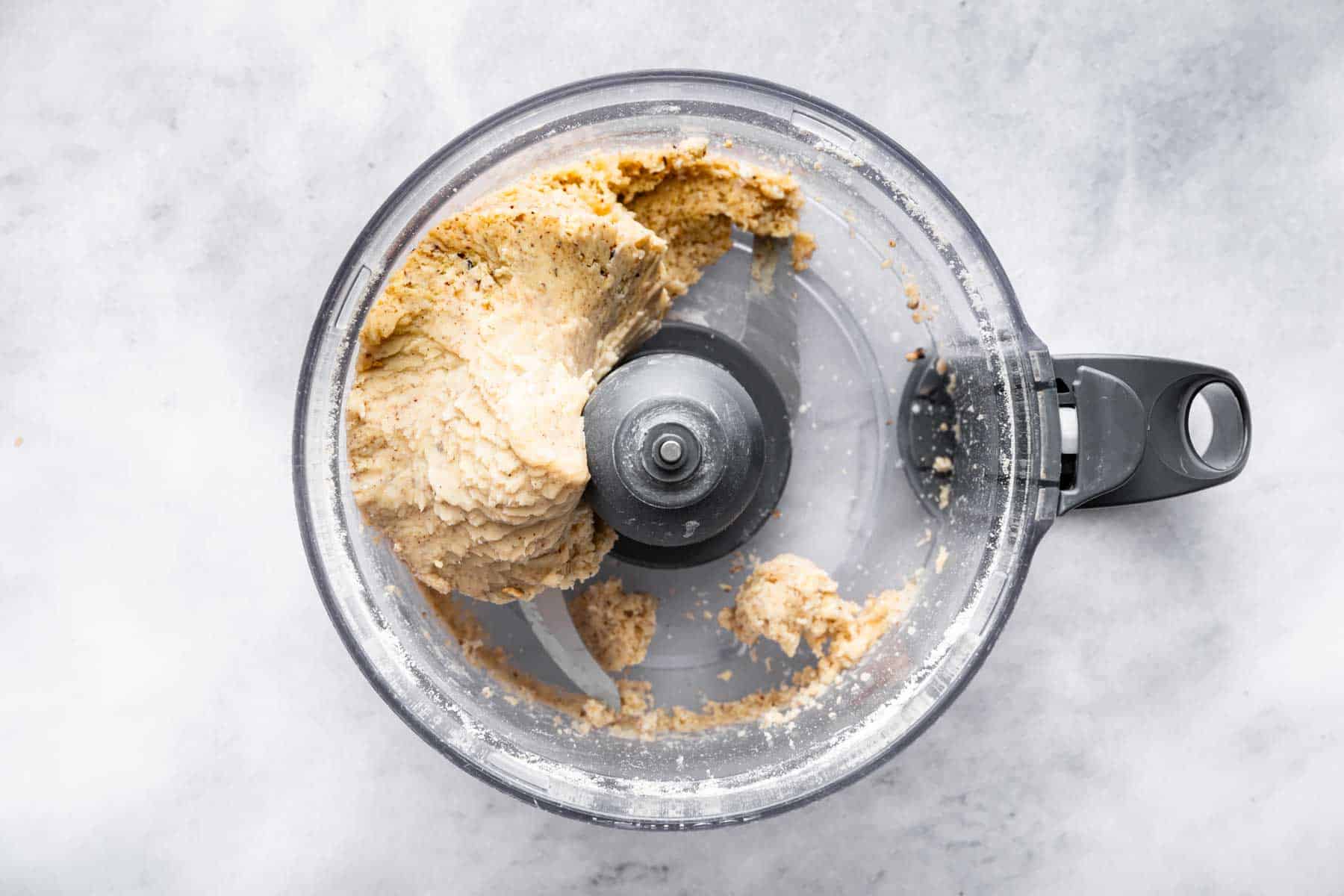 Food processor bowl with brown lump of dough.