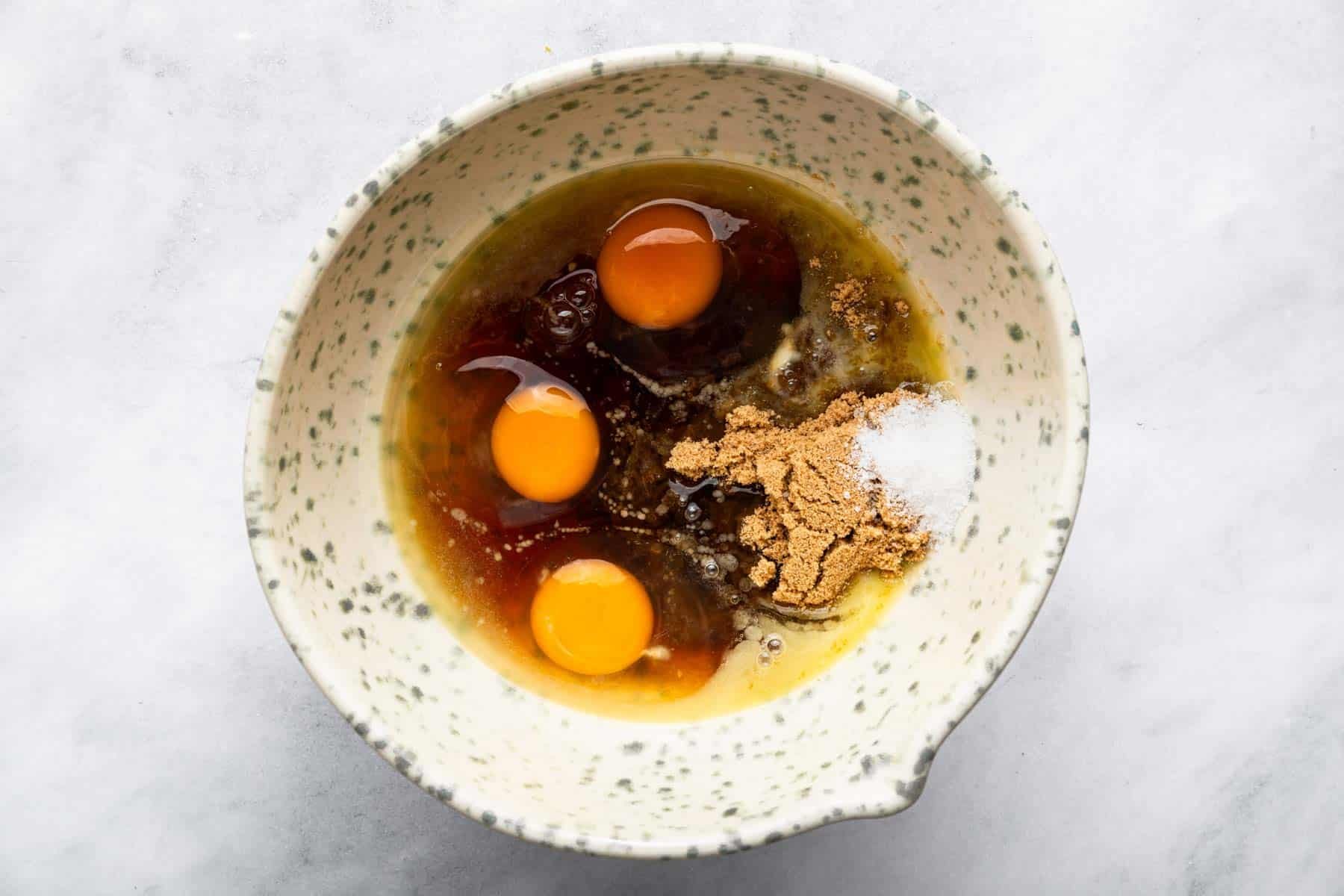 Three eggs in a brown liquid batter in speckled bowl.