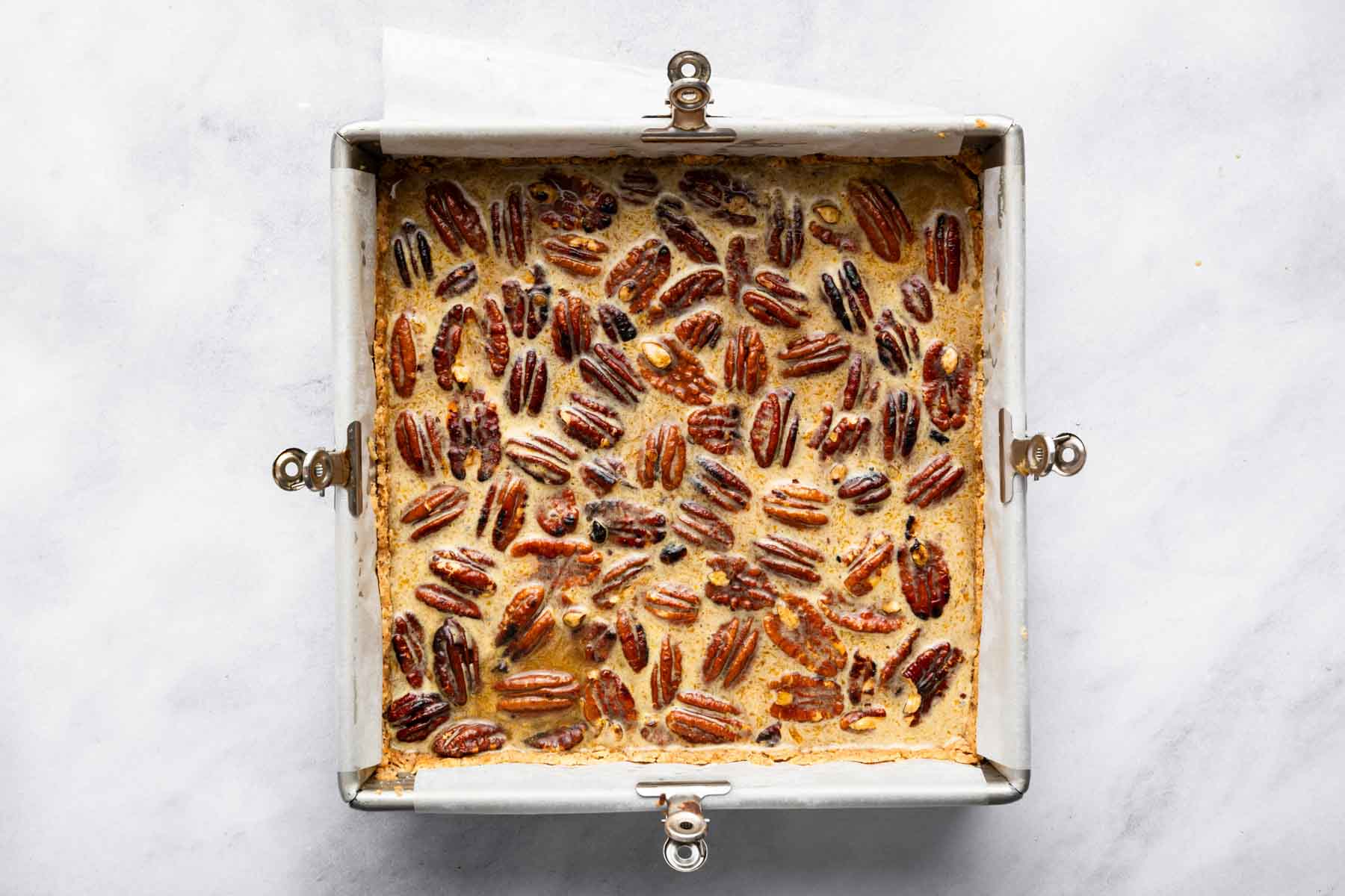 Pecan halves in a tan batter in a square pan.
