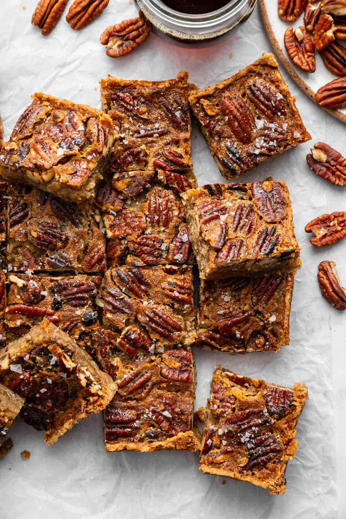 Twelve cut pecan pie bars on table with cup of maple syrup next to them.
