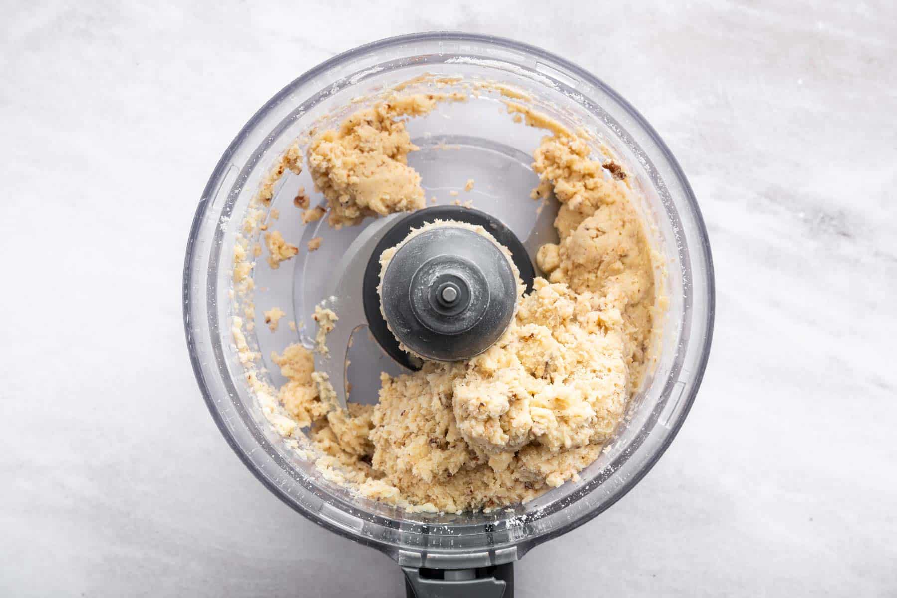 Pale yellow dough with brown specks clumped around blade of food processor.