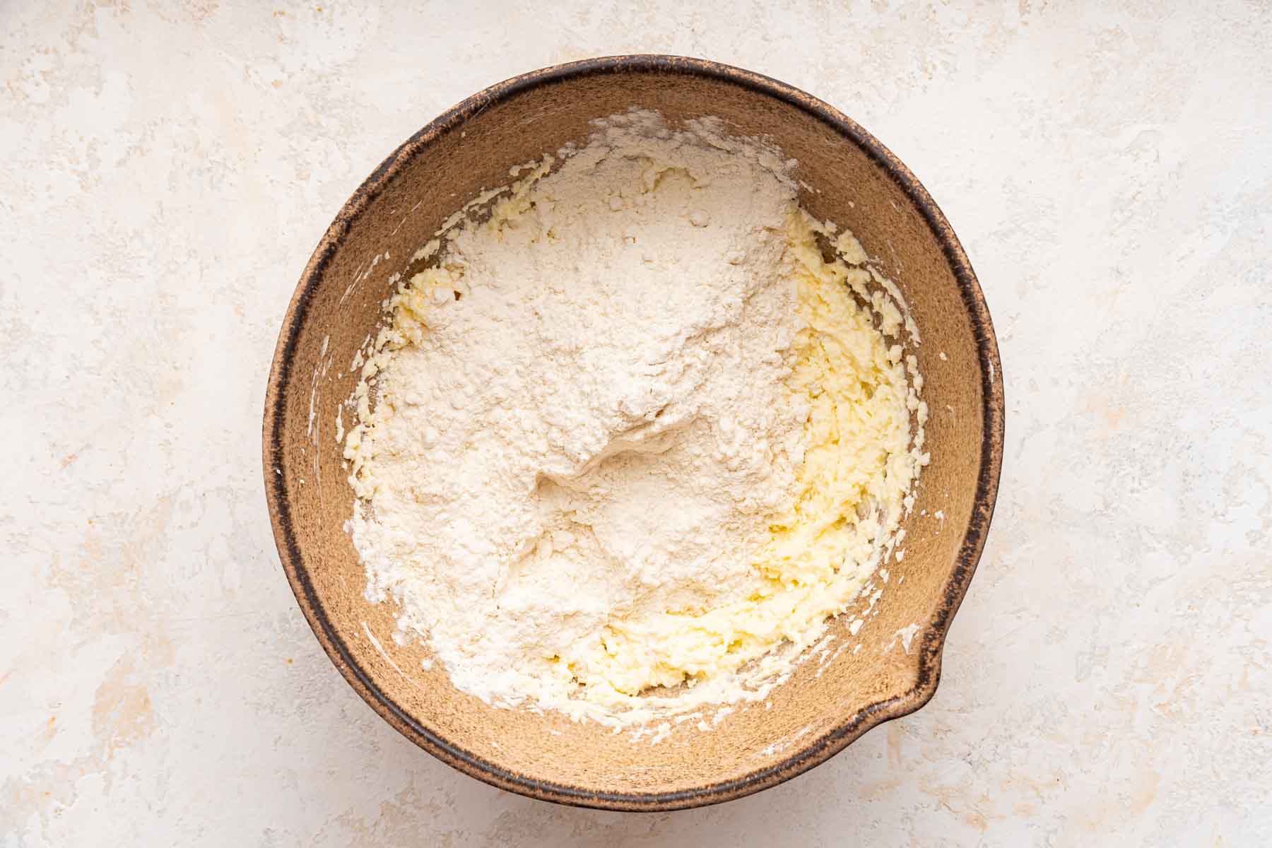 Brown bowl with flour over yellow batter.