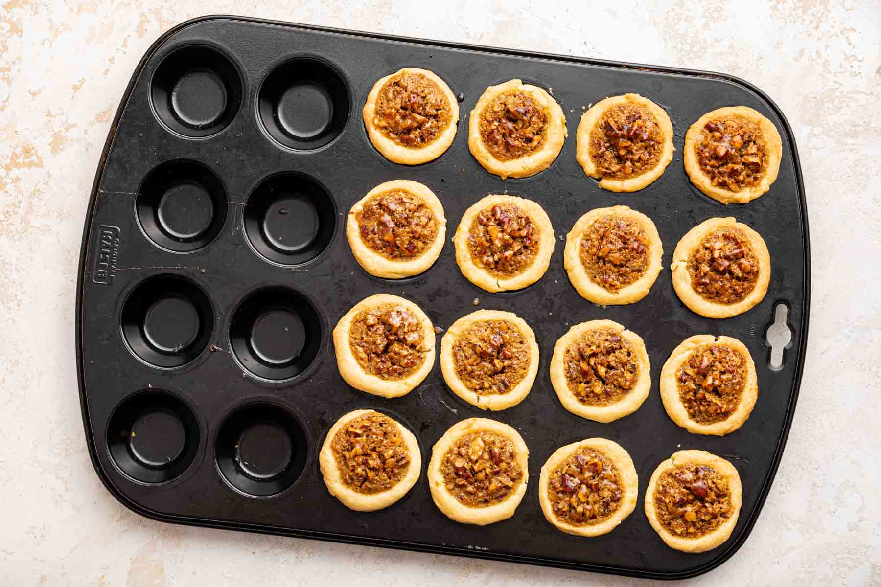 Sixteen mini pecan tastes in a muffin pan, freshly baked.