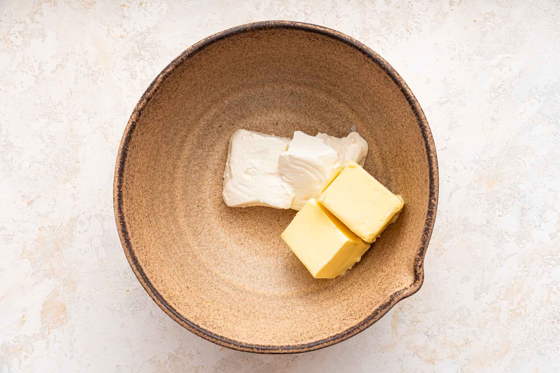 Butter and cream cheese in a brown mixing bowl.