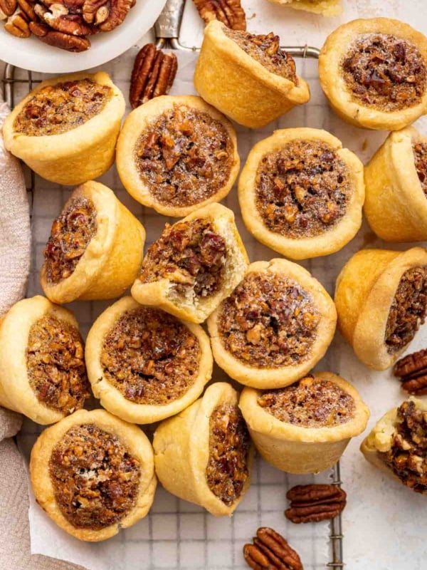 Pile of pecan tassies cookies with brown filling and pecans on side.