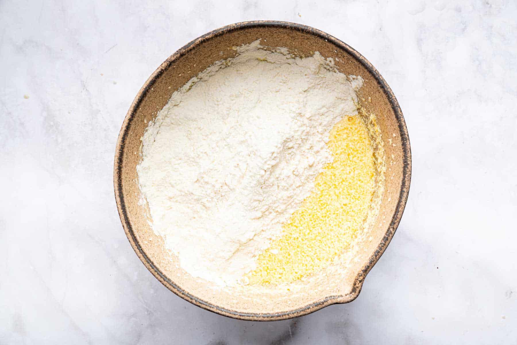 Bowl with yellow cake batter and white flour on top, before being stirred in.