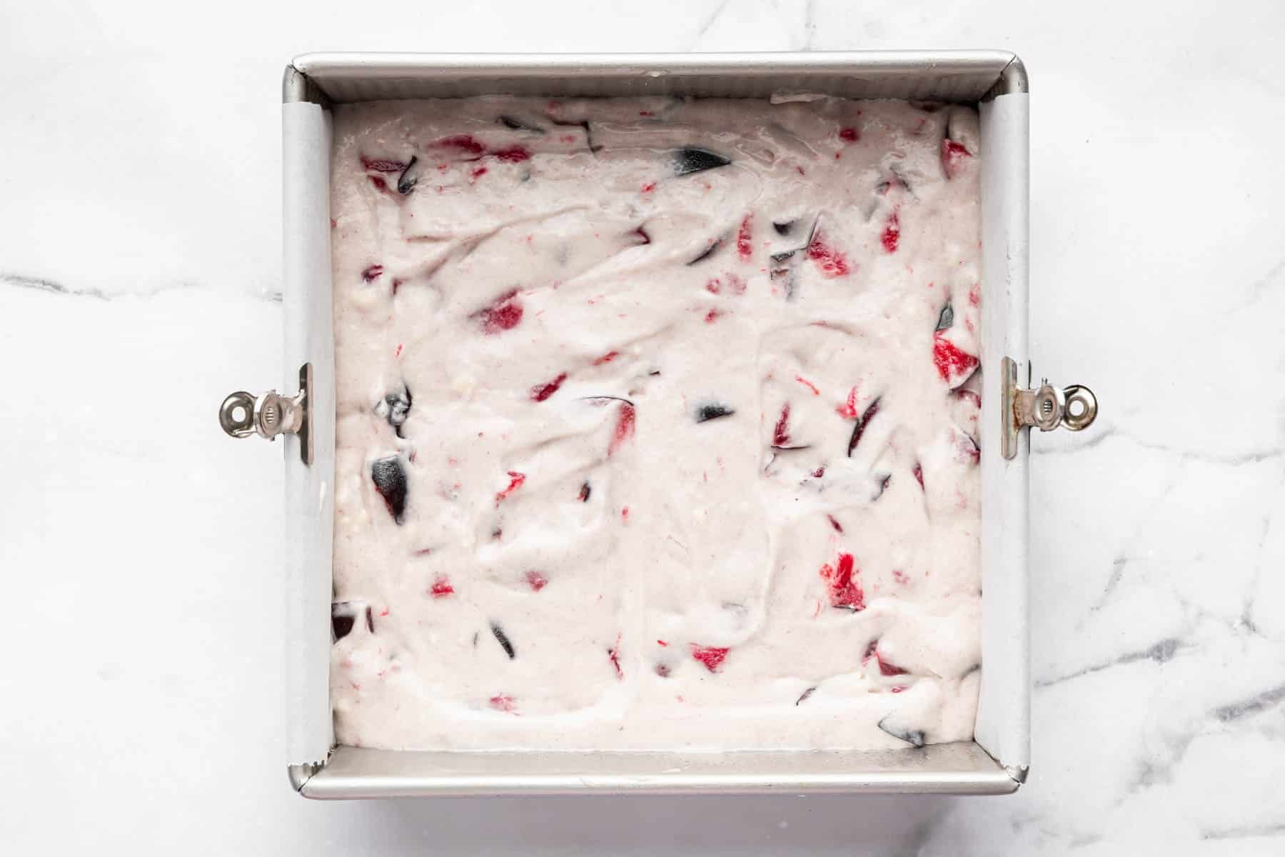 White raw batter in a square pan with chunks of red and purple fruit.