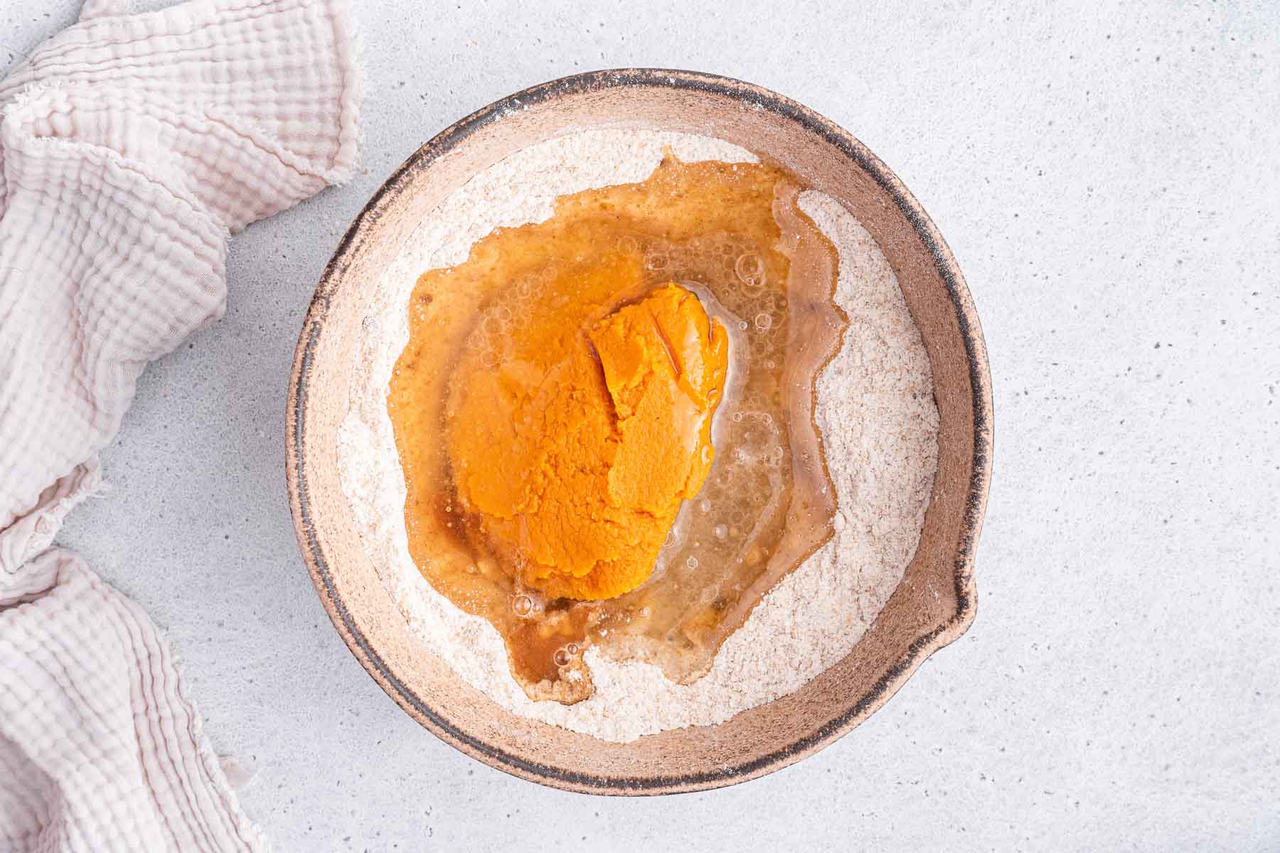 Pumpkin and oil in earthenware bowl with flour and sugars.