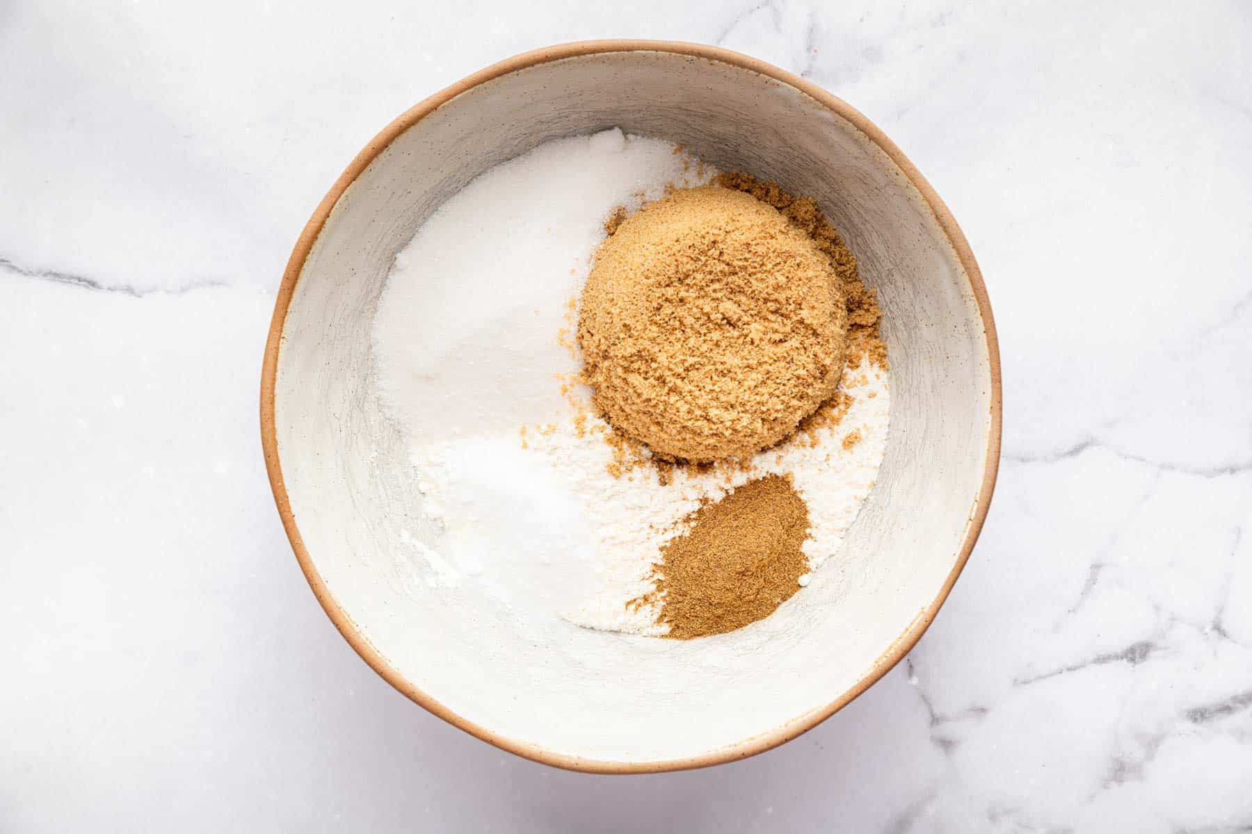 White bowl with flour, white sugar, brown sugar, and brown spices.