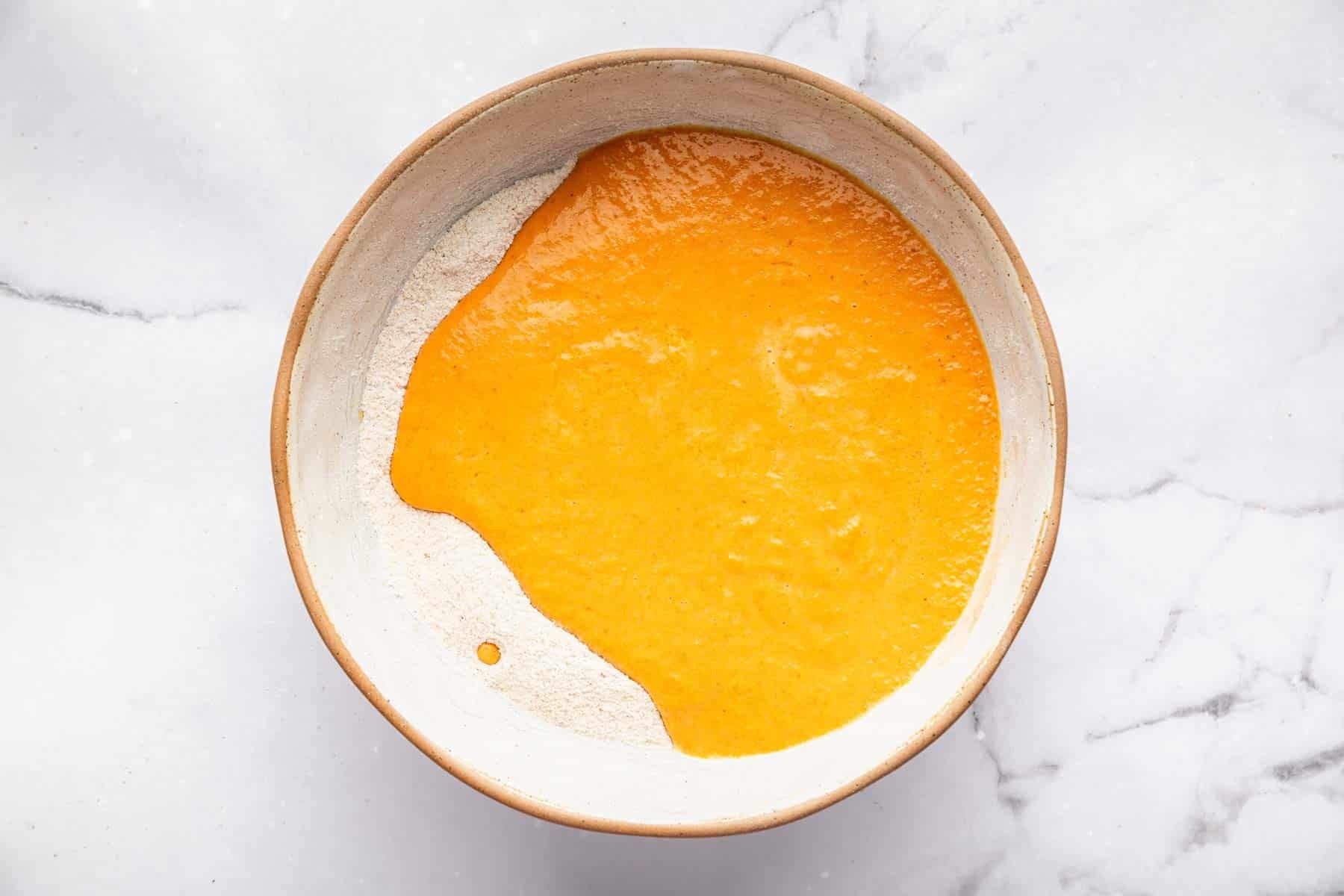 Bright orange batter poured over flour in a mixing bowl.