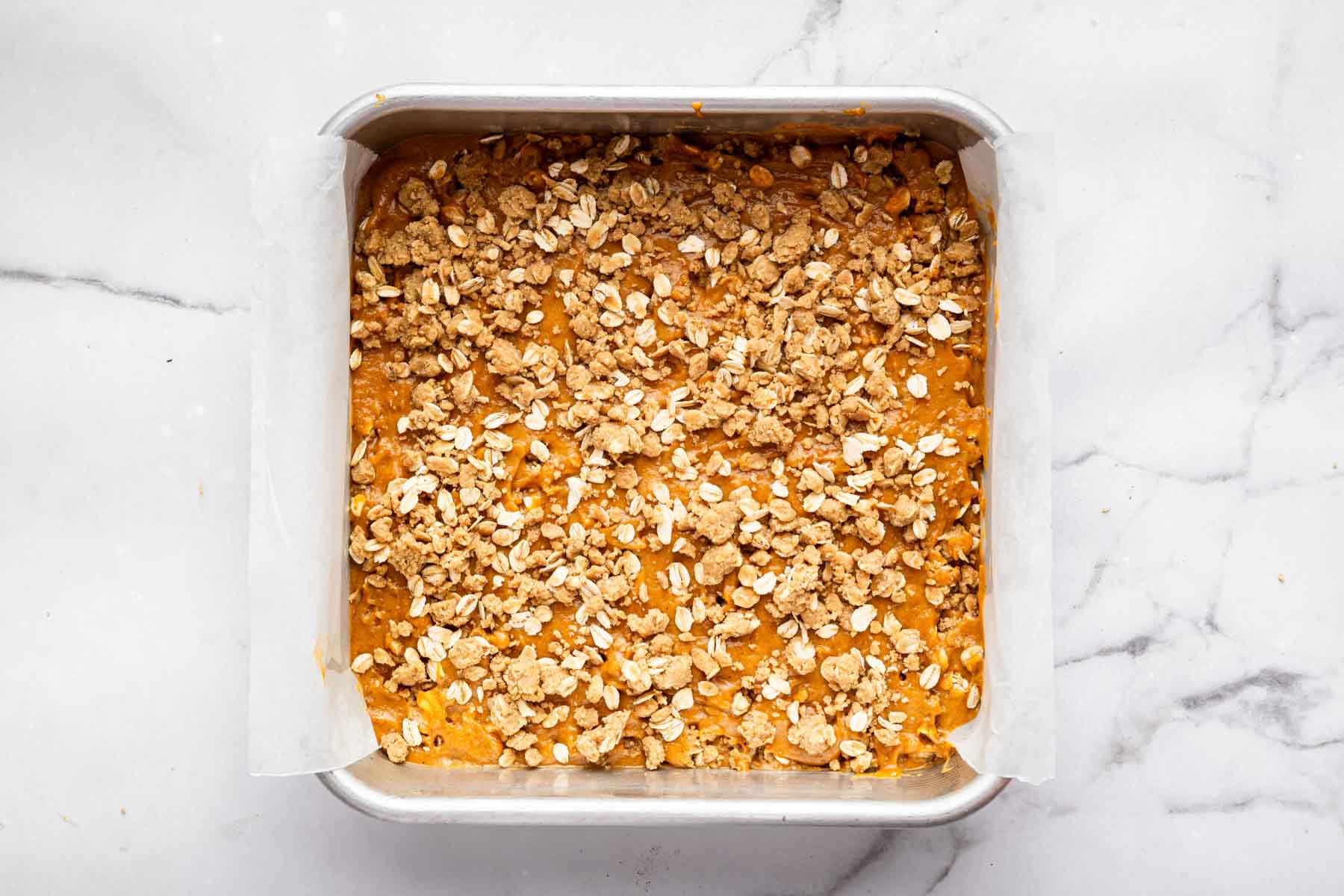 Pumpkin coffee cake with crumb topping in a square pan before baking.