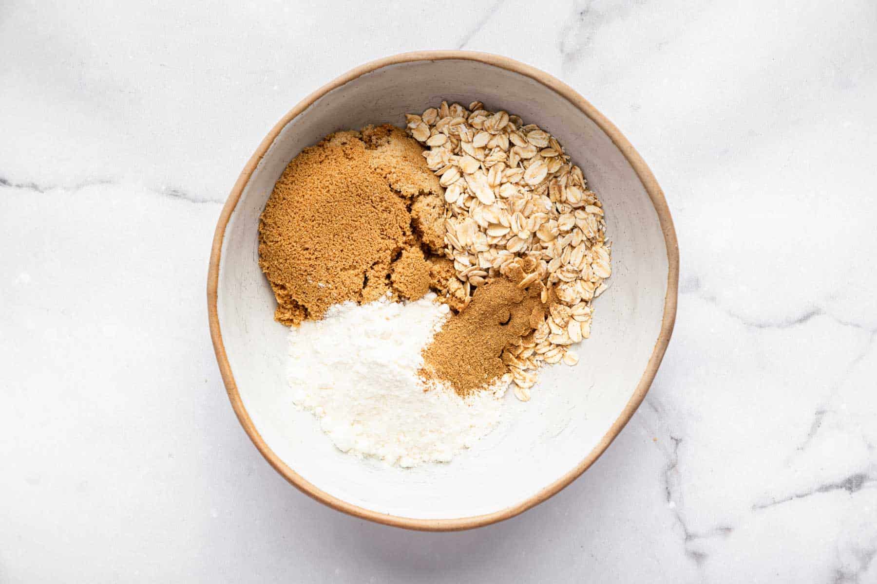 White bowl with brown sugar, oats, flour, and spices.