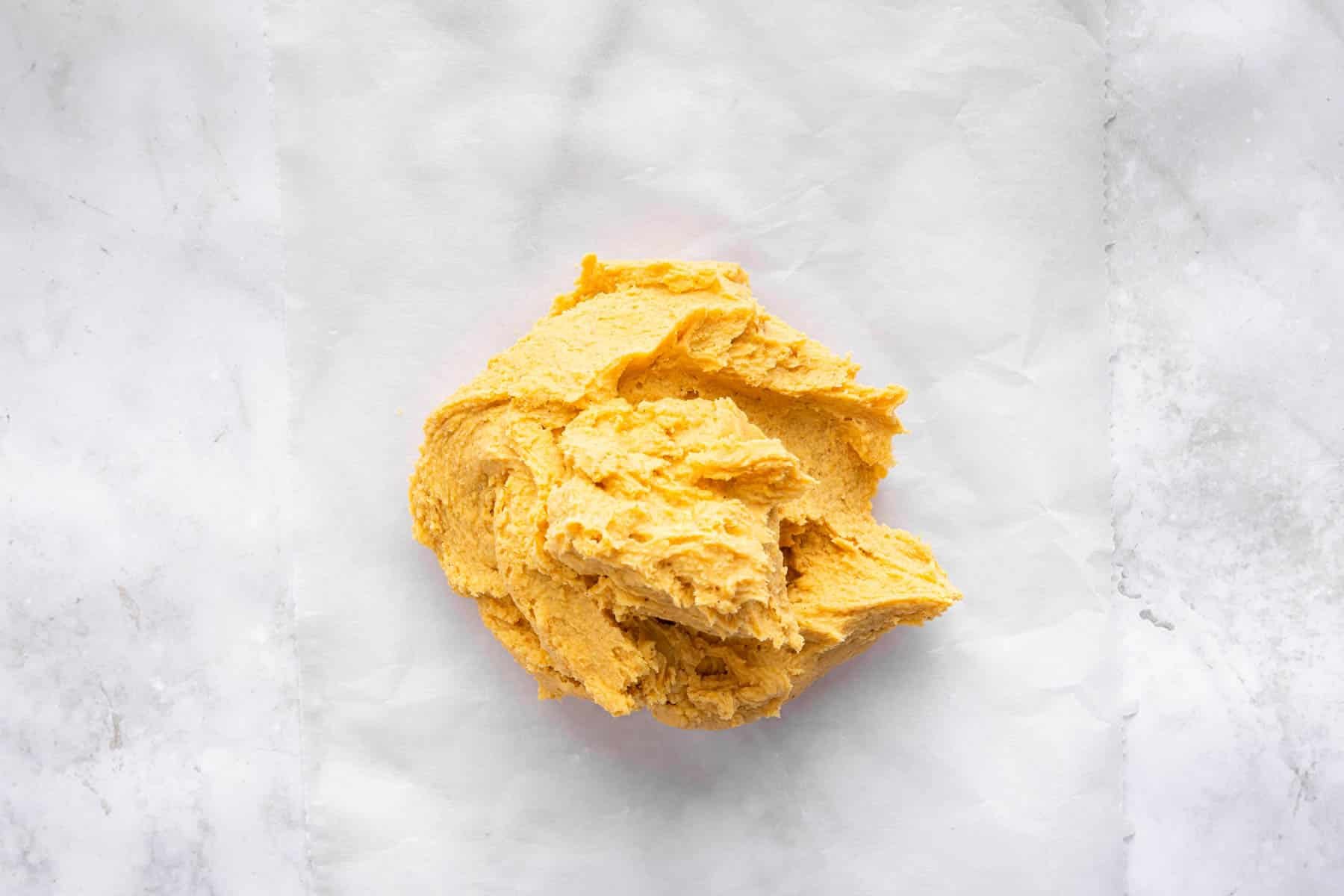 Ball of orange dough on a marble cutting board.