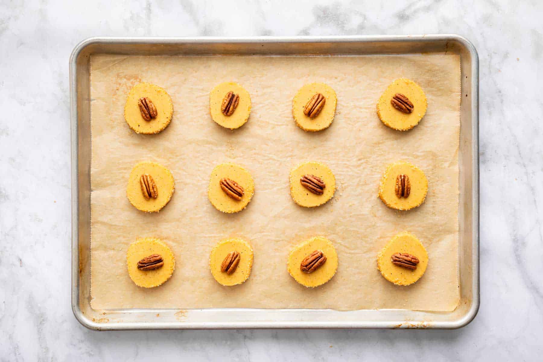 Twelve pumpkin shortbread cookies with a glazed pecan on top.