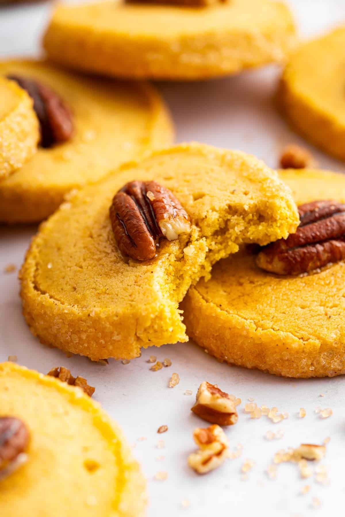 One pumpkin shortbread cookie with bite missing leaning on another cookie.