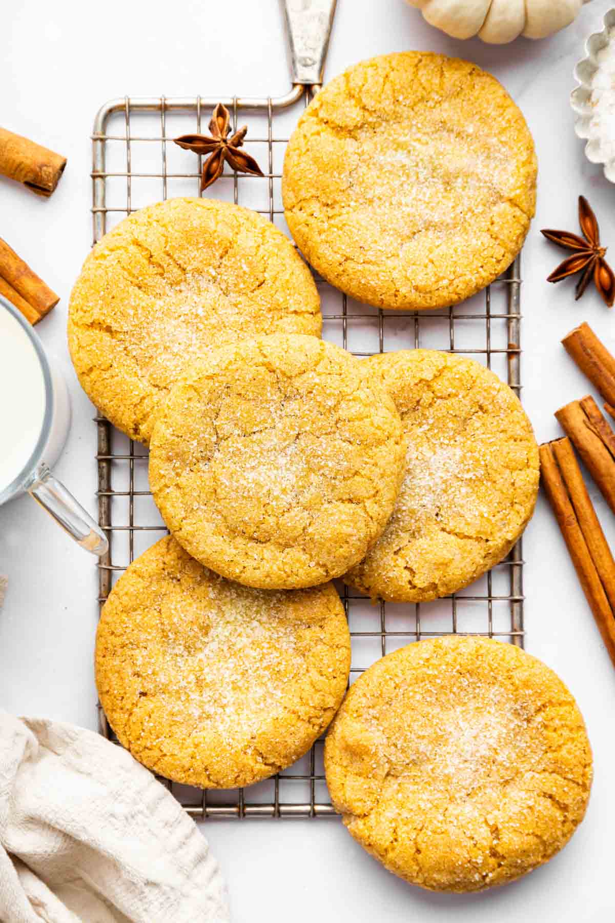 Overhead image of pumpkin sugar cookies on a wire rack with cinnamon sticks.