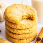 Orange pumpkin sugar cookies stacked up with bite missing from top cookie.