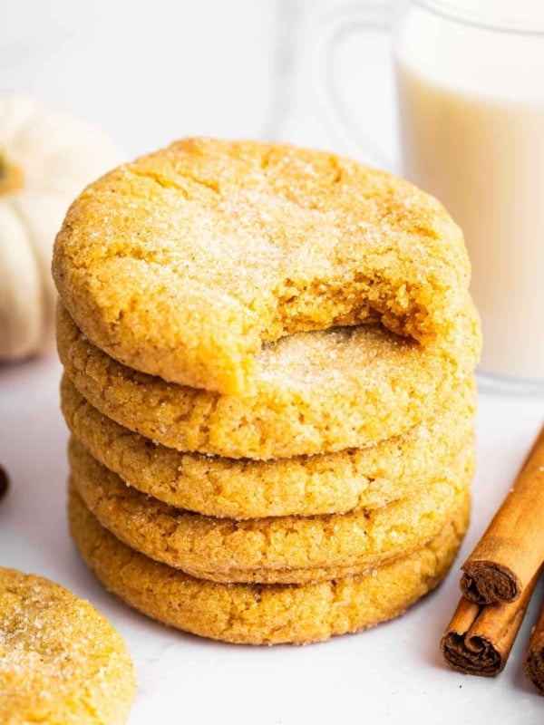 Orange pumpkin sugar cookies stacked up with bite missing from top cookie.