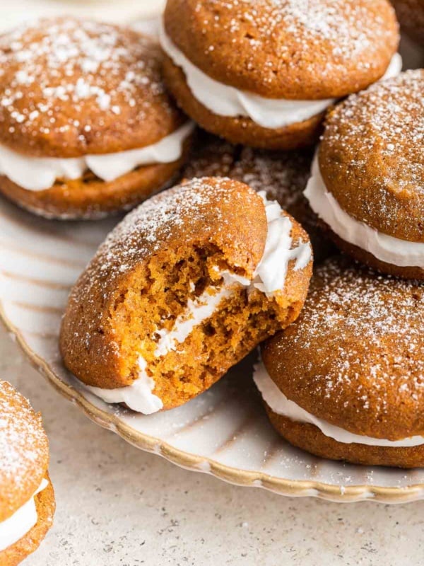 Orange pumpkin whoopie pies on white plate.