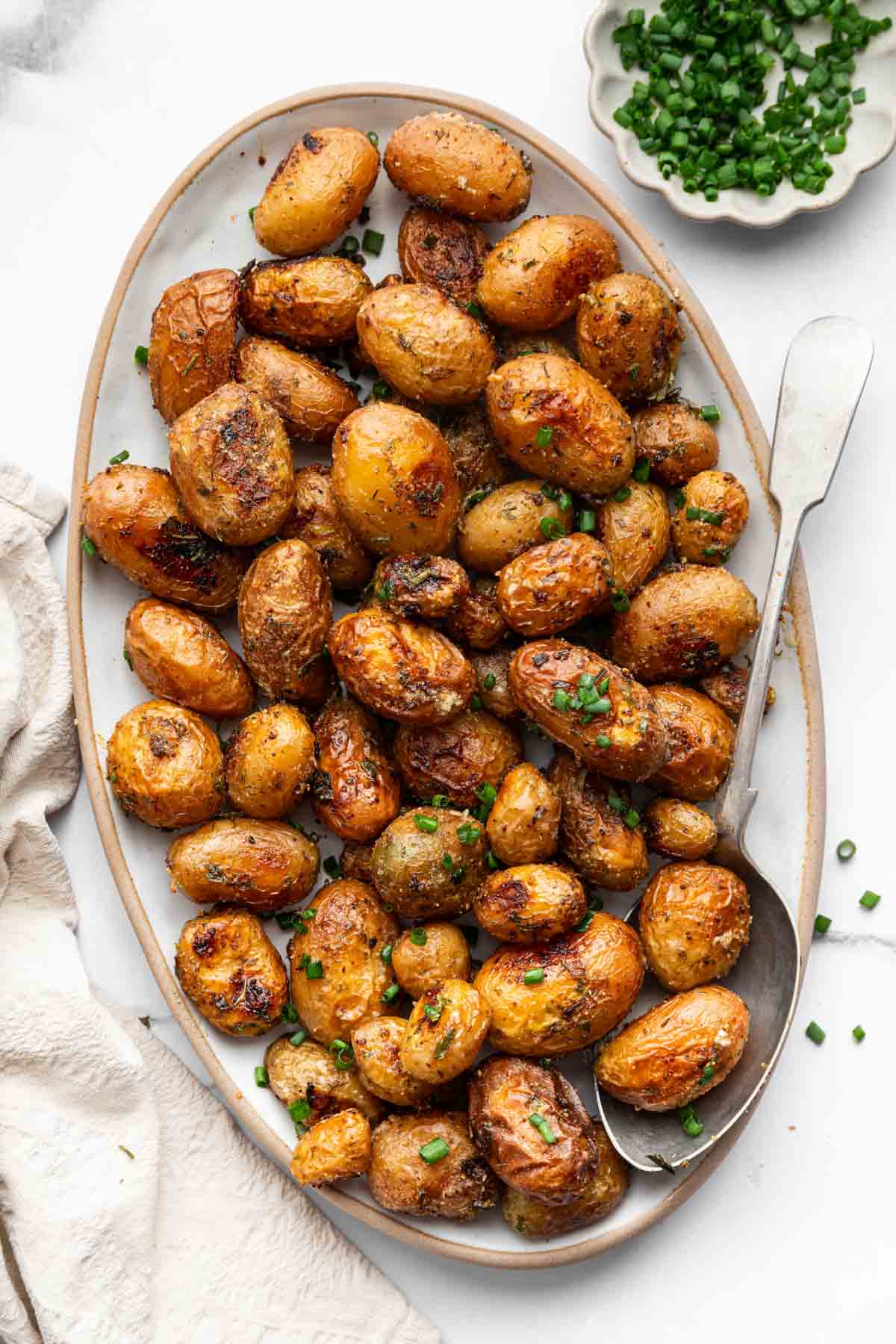 Vertical image of ranch potatoes on oval platter with chives.
