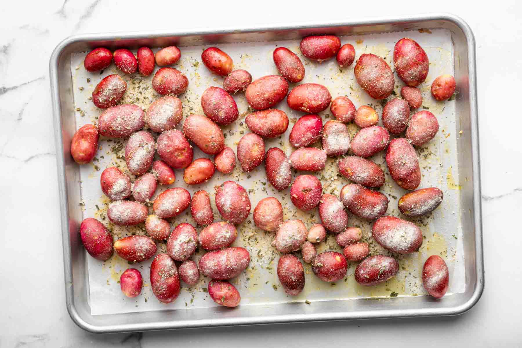 Red potatoes with white powder on them on a baking sheet.