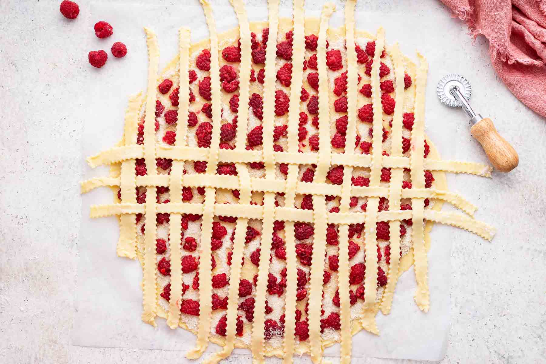 The beginning of a lattice crust on a round pie crust with fresh raspberries.