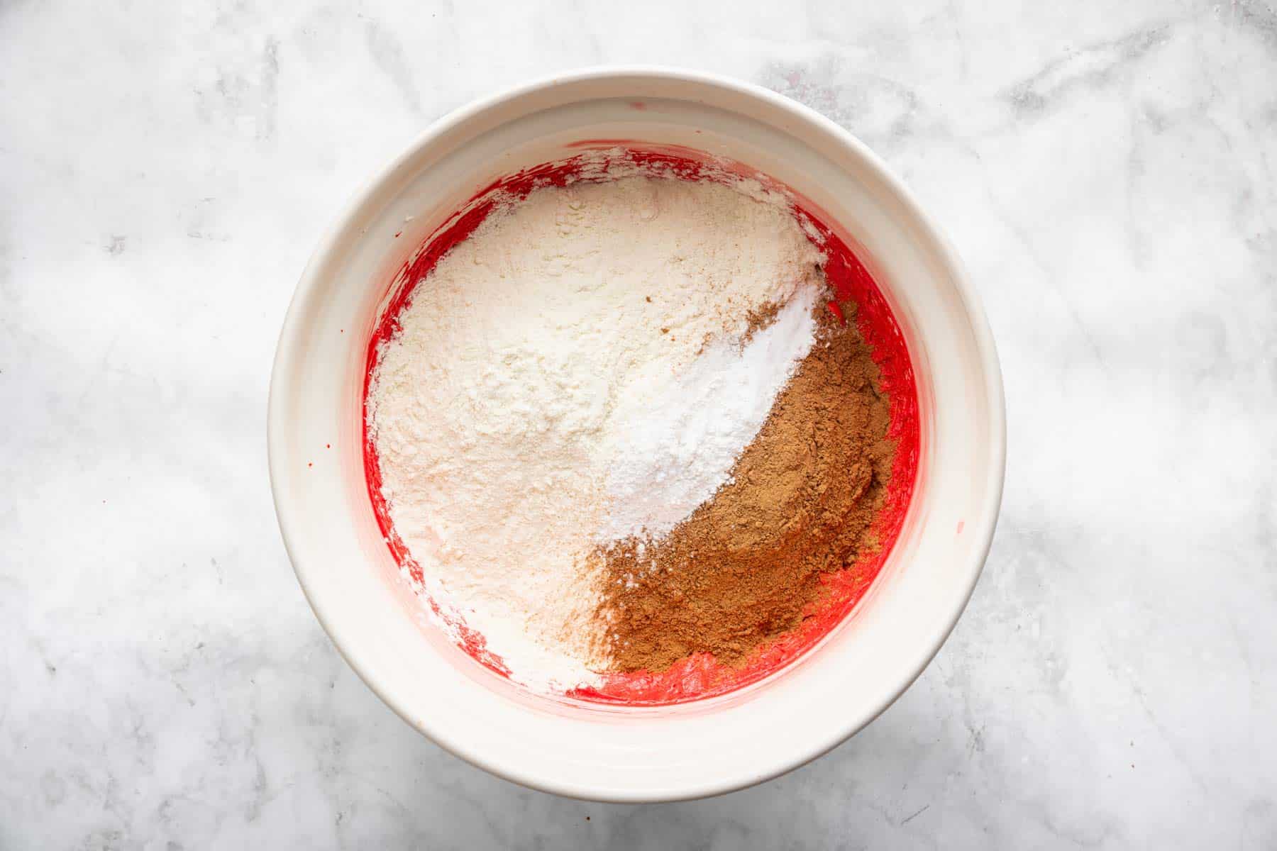 Red batter with flour and cocoa powder sprinkled on top.