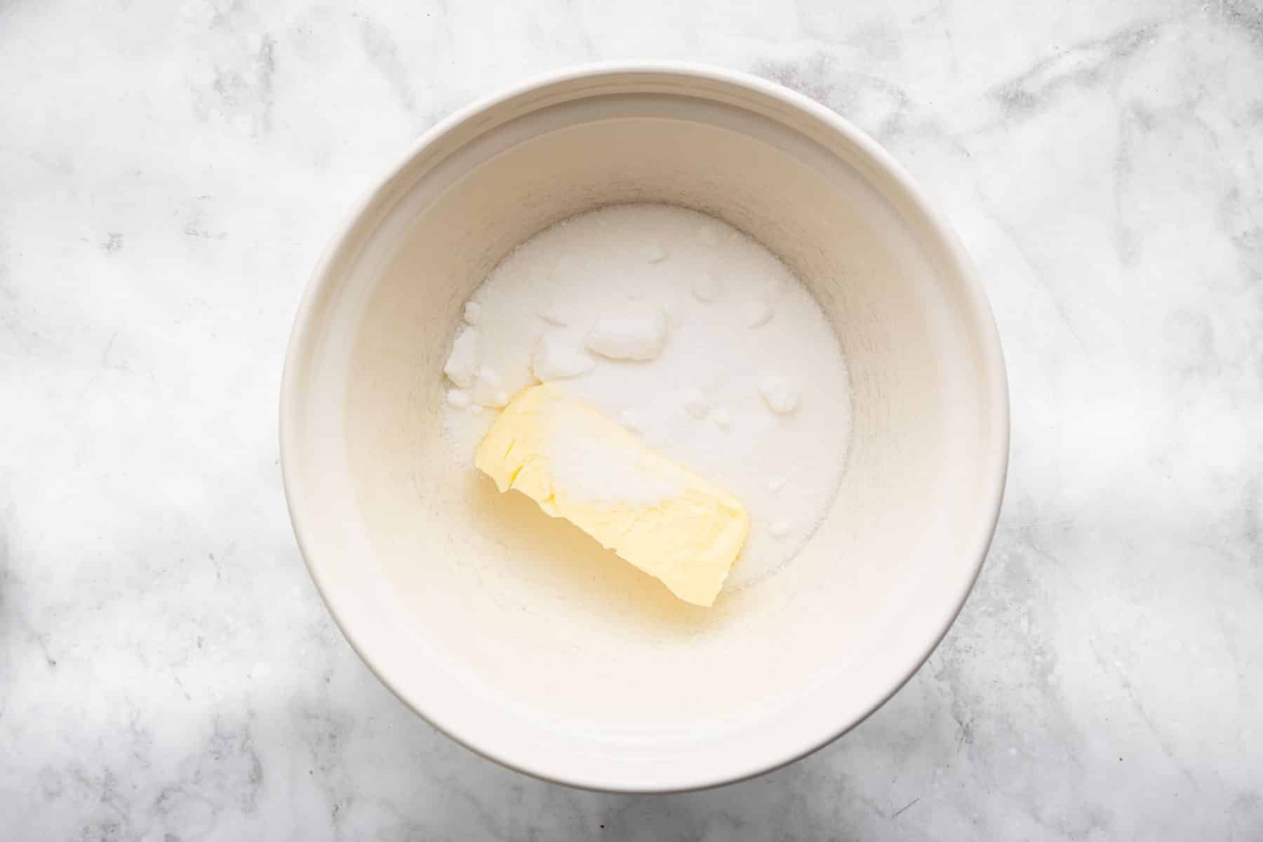 White bowl with whole stick of butter and granulated sugar sprinkled on top.