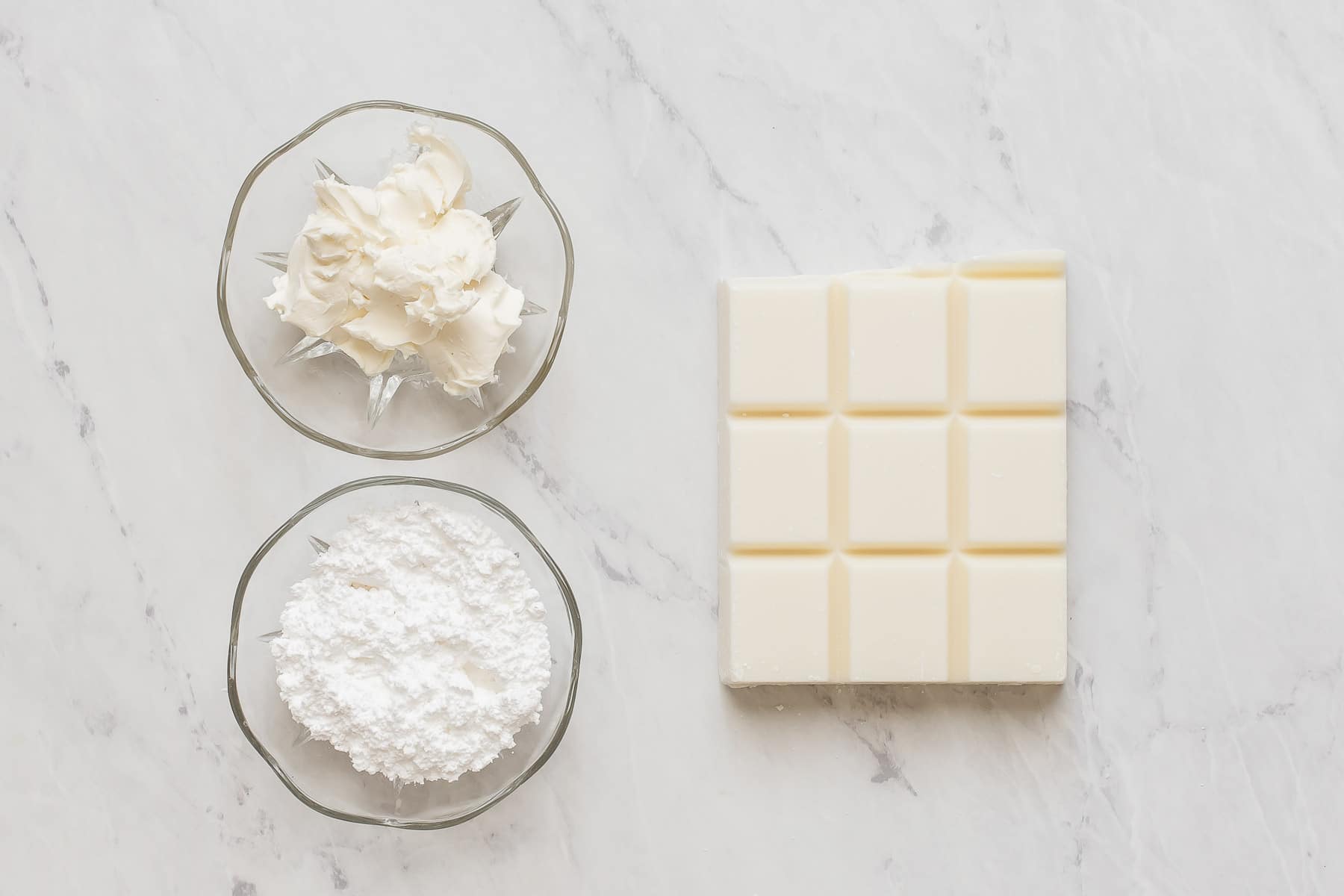 White chocolate, cream cheese, and powdered sugar on white table.