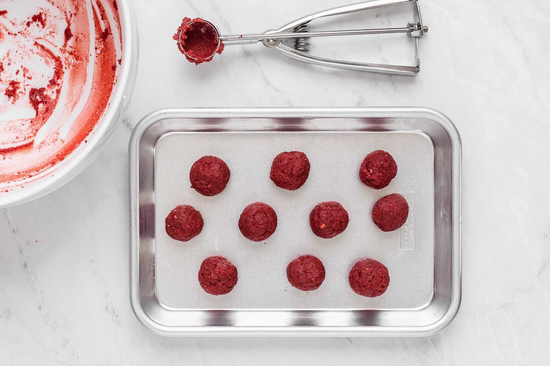 Ten red velvet cake pops on a cookie sheet.