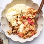 Up-close shot of rhubarb crisp on plate with ice cream and spoon.