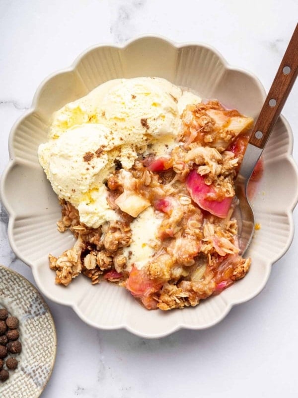 Up-close shot of rhubarb crisp on plate with ice cream and spoon.