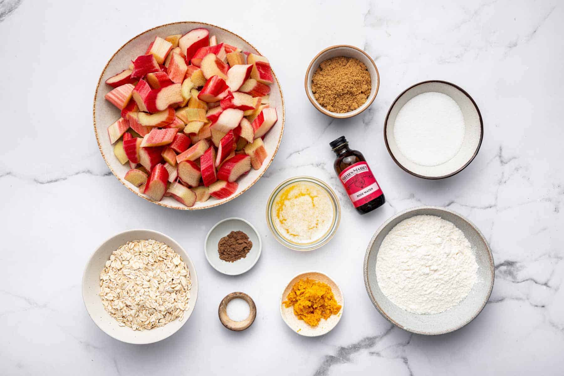Bowl of sliced fruit, sugar, rose water extract, and flour on counter.