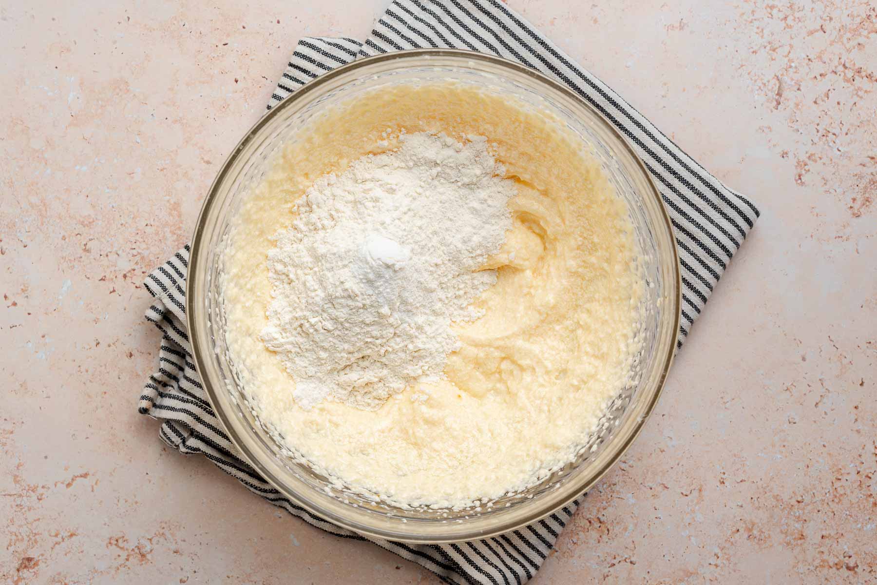 Flour sprinkled over cake batter in glass bowl.