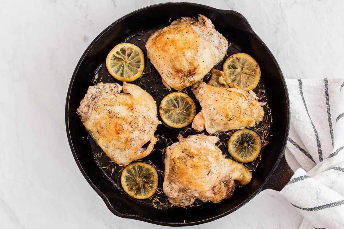 chicken thighs in a cast iron skillet with lemon slices and rosemary