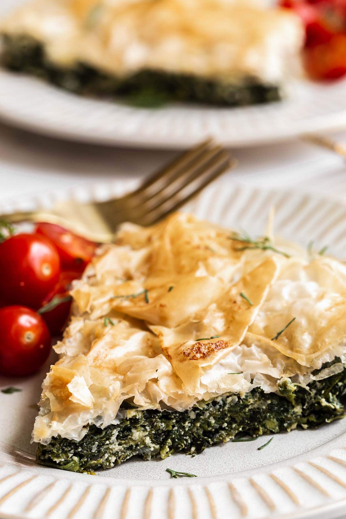 Slice of skillet spanakopita on white plate with fresh cherry tomatoes on the side.