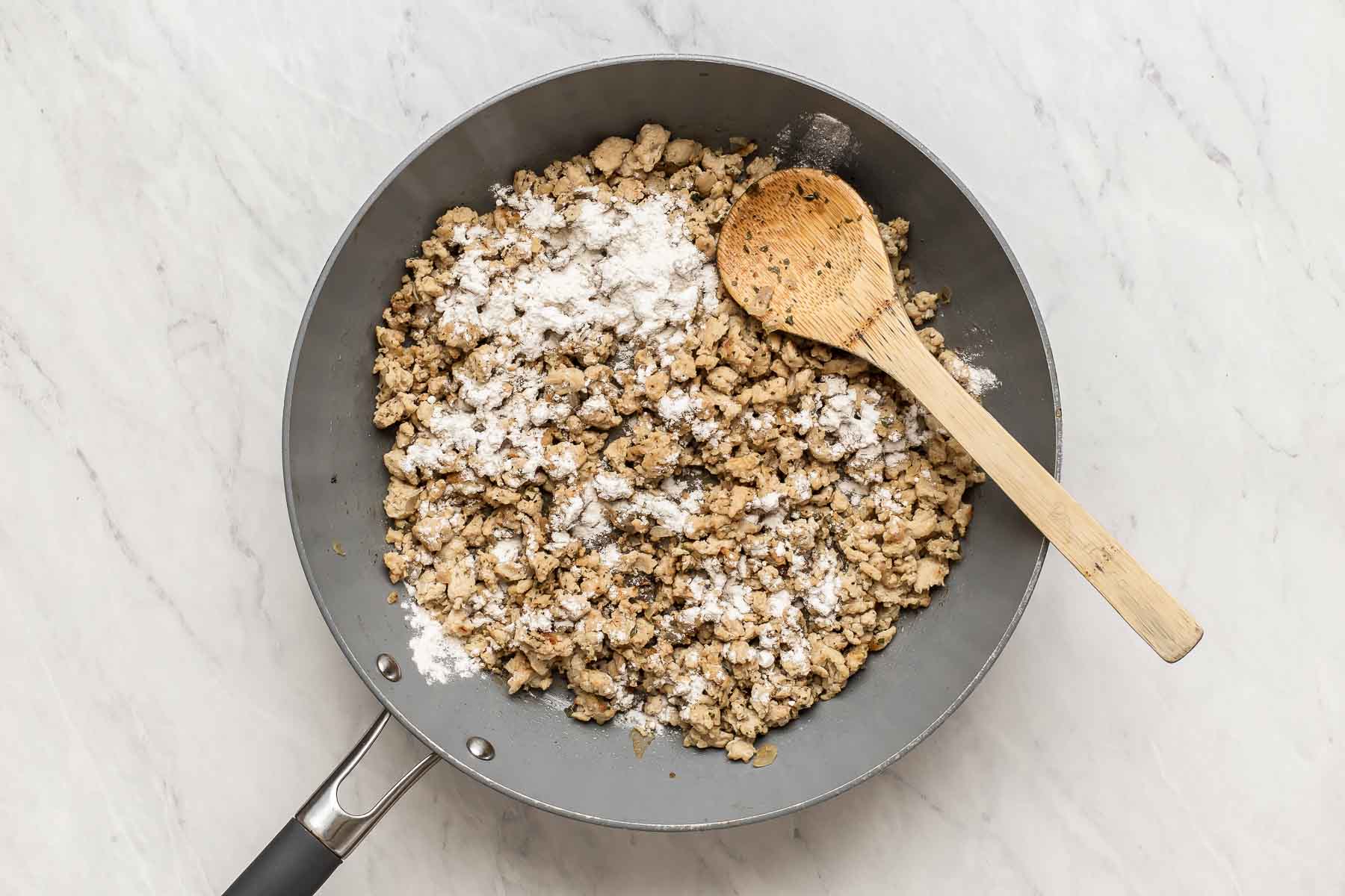 Adding flour to skillet with ground chicken.