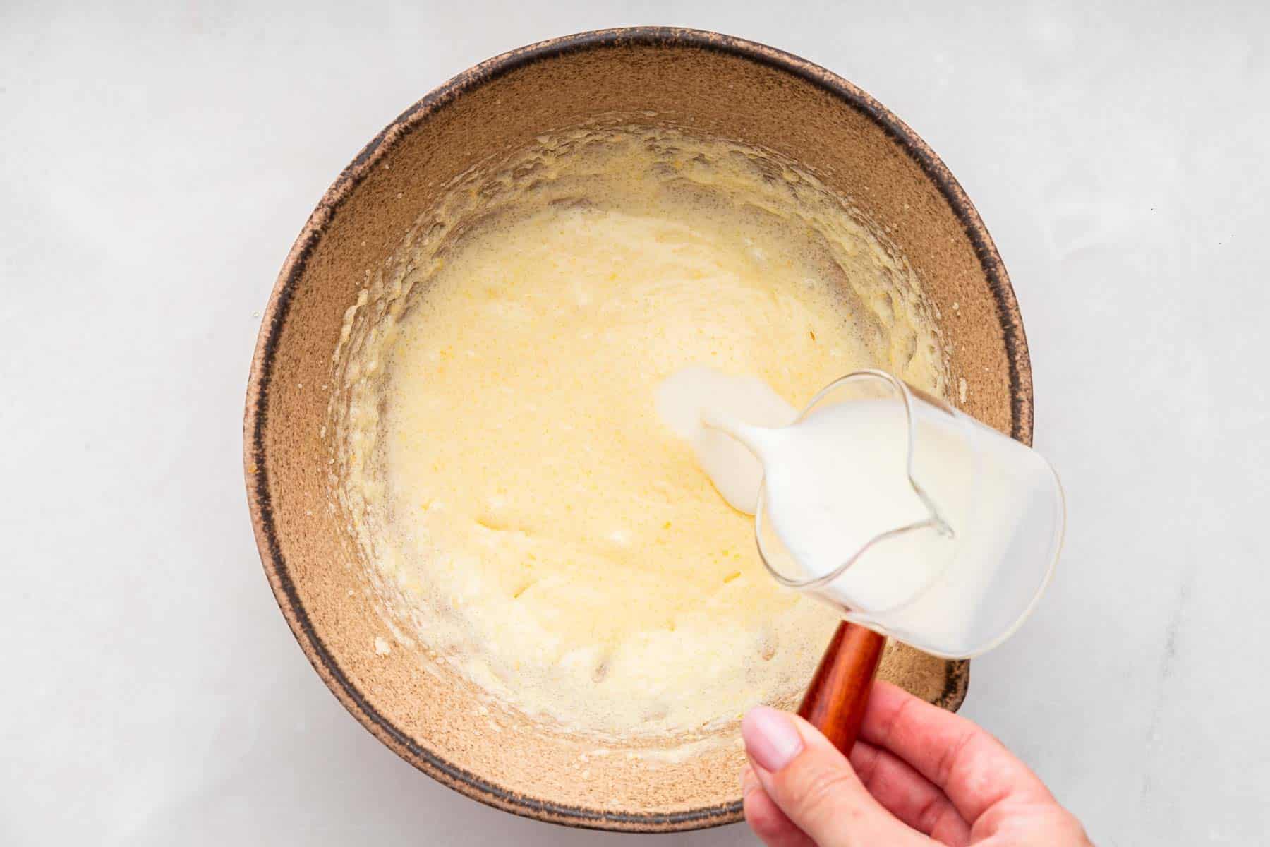 Hand pouring buttermilk into yellow batter.