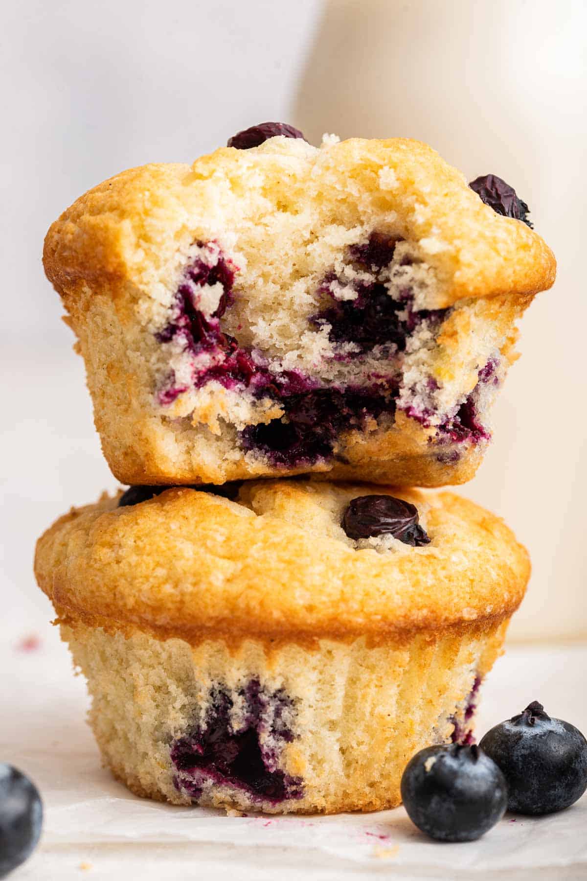 Two blueberry muffins stacked on top of each other, bite missing from top muffin.
