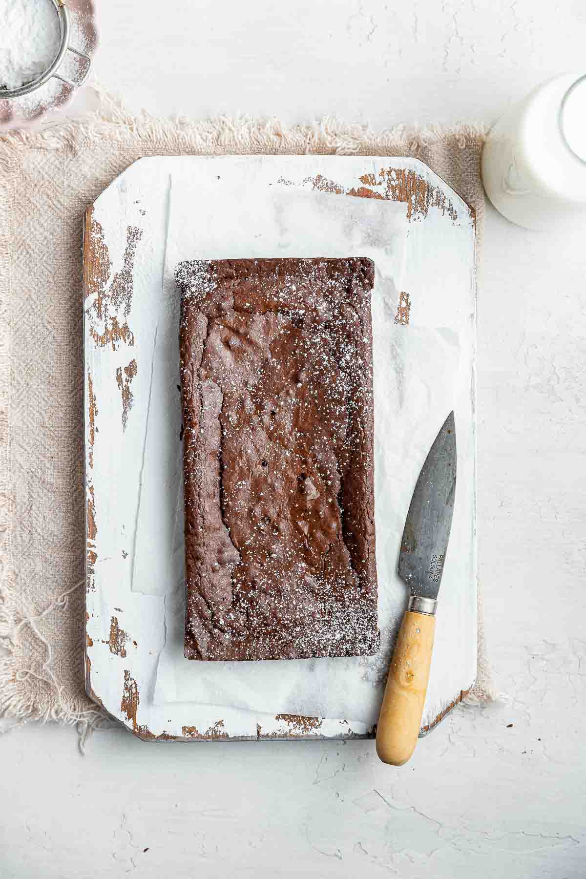 Long rectangular brownie chunk on white plate with knife alongside.