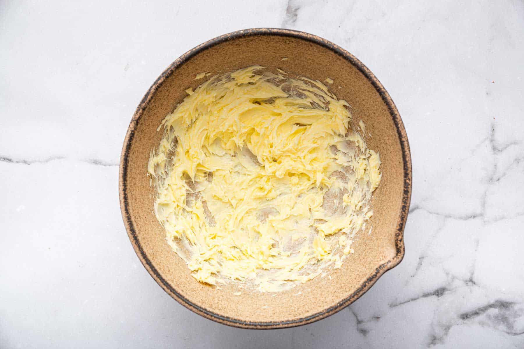 Softened butter and sugar mixed up in a brown mixing bowl.