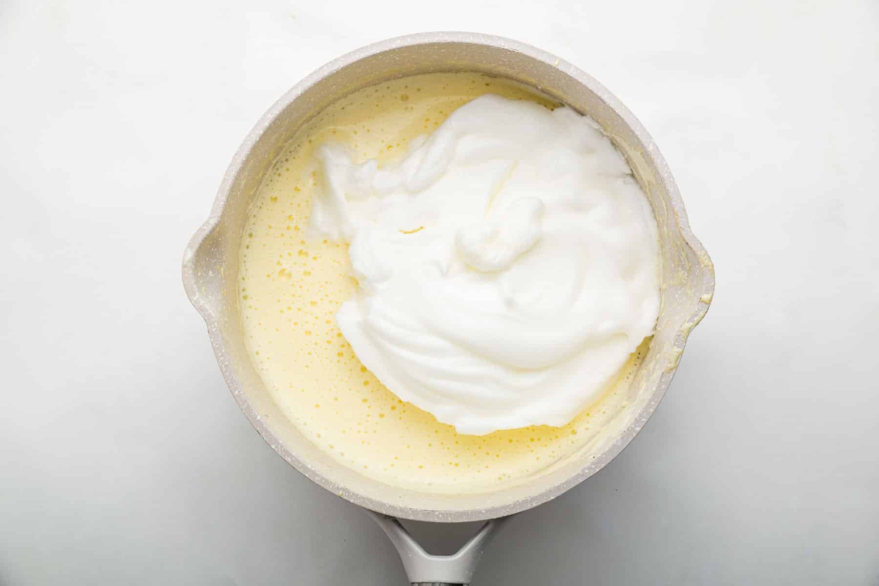 Fluffy egg whites being folded into pale yellow batter in pan.