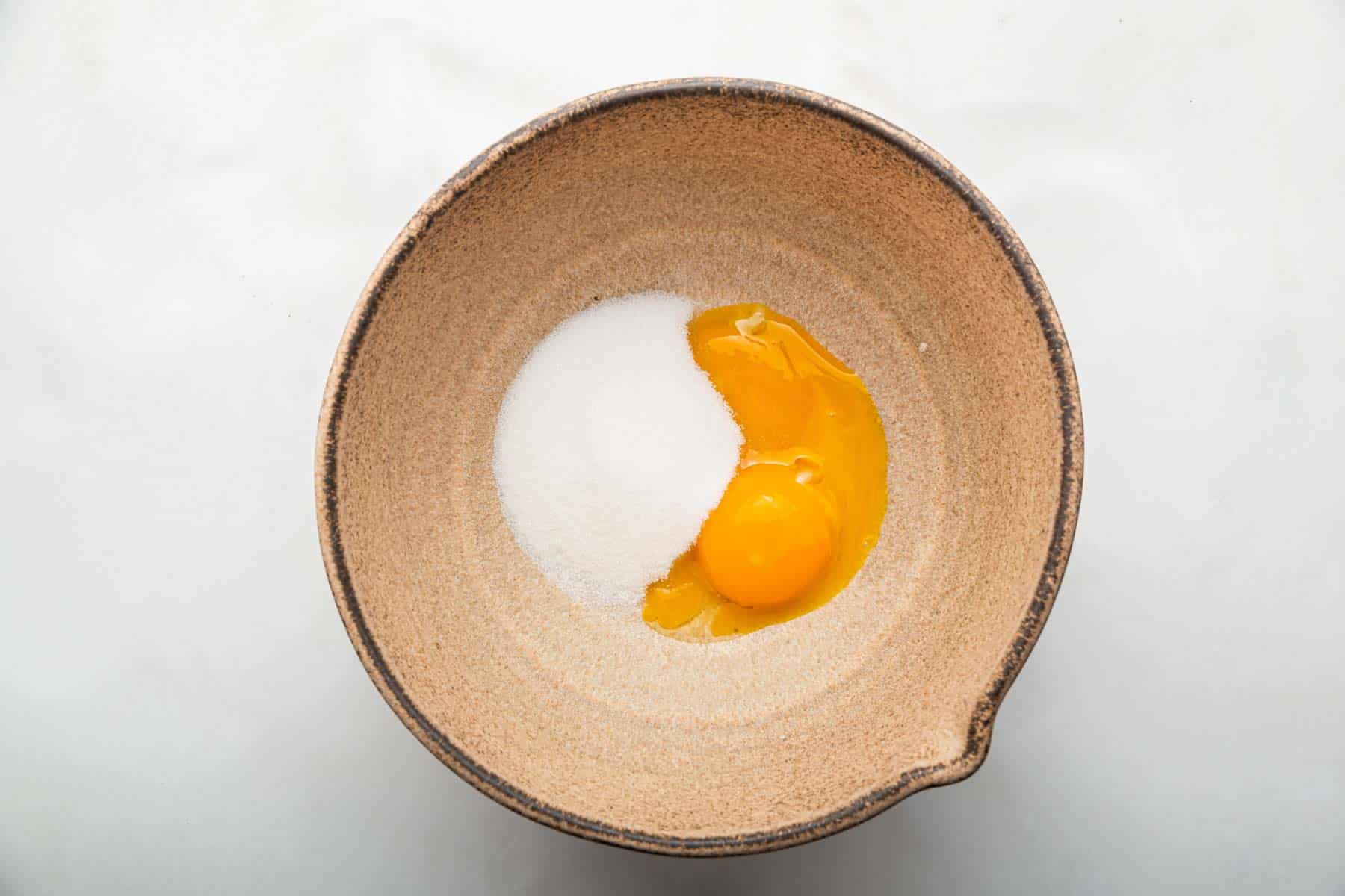 Egg yolks and white sugar in a brown bowl.