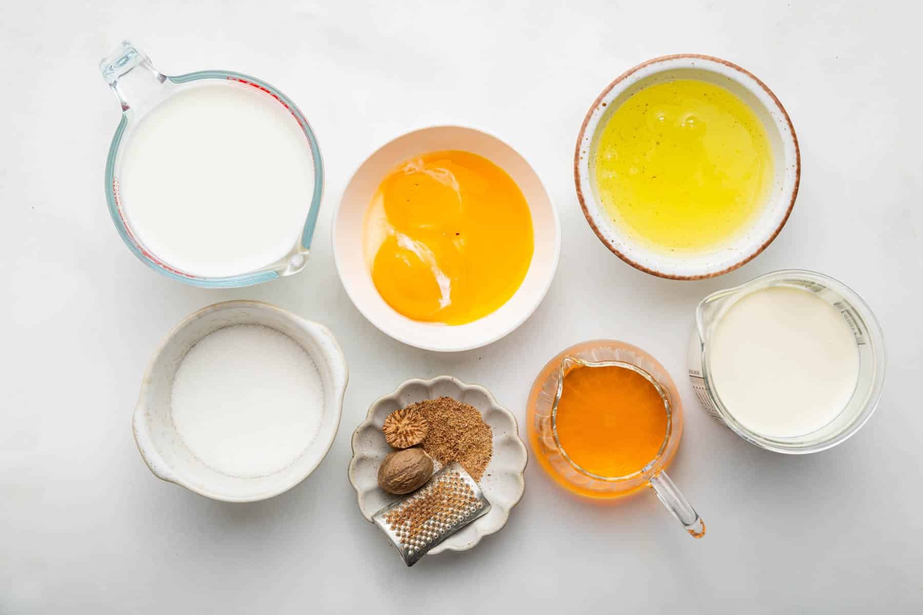 Small bowls of dairy products, eggs, alcohol and nutmeg on kitchen counter.