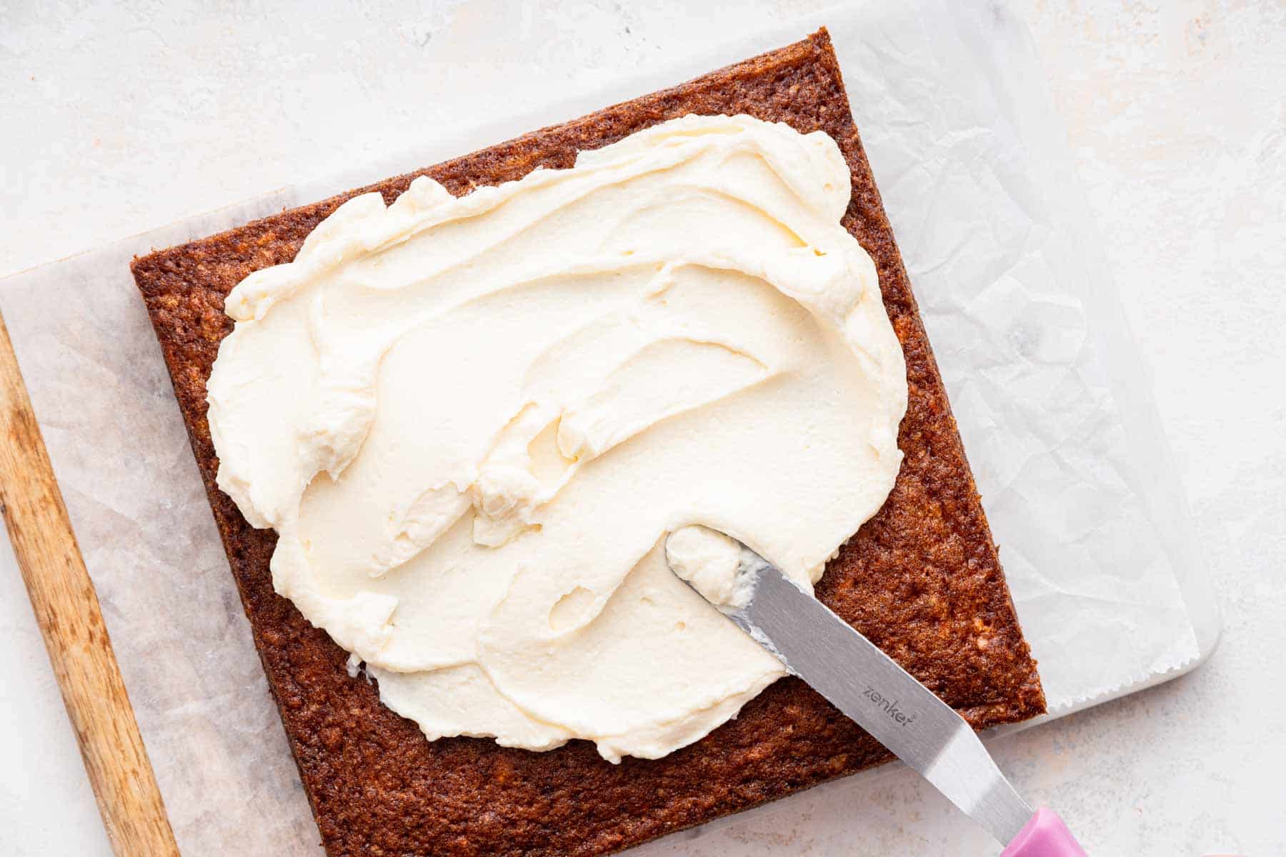 Spatula spreading frosting on a square pastry.