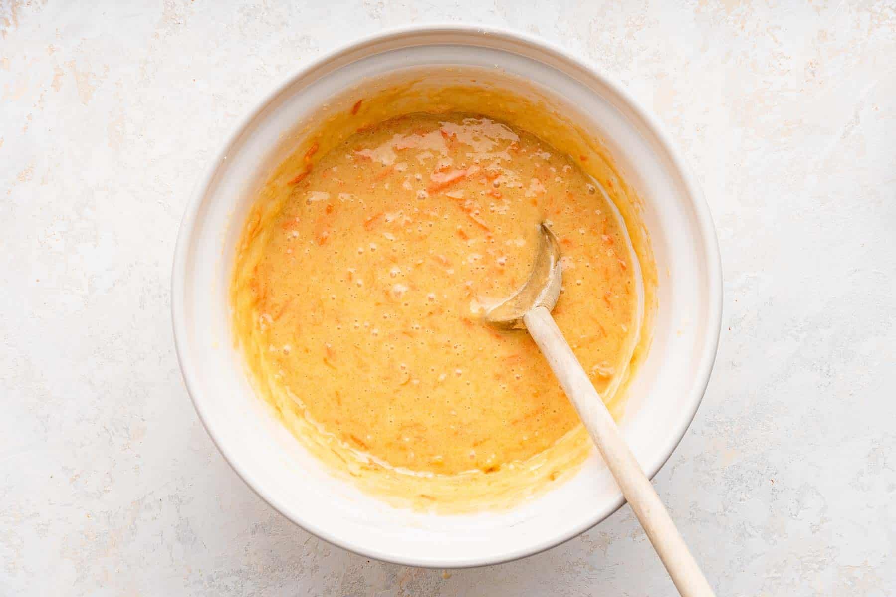 White bowl with light yellow to orange batter and spoon in it.