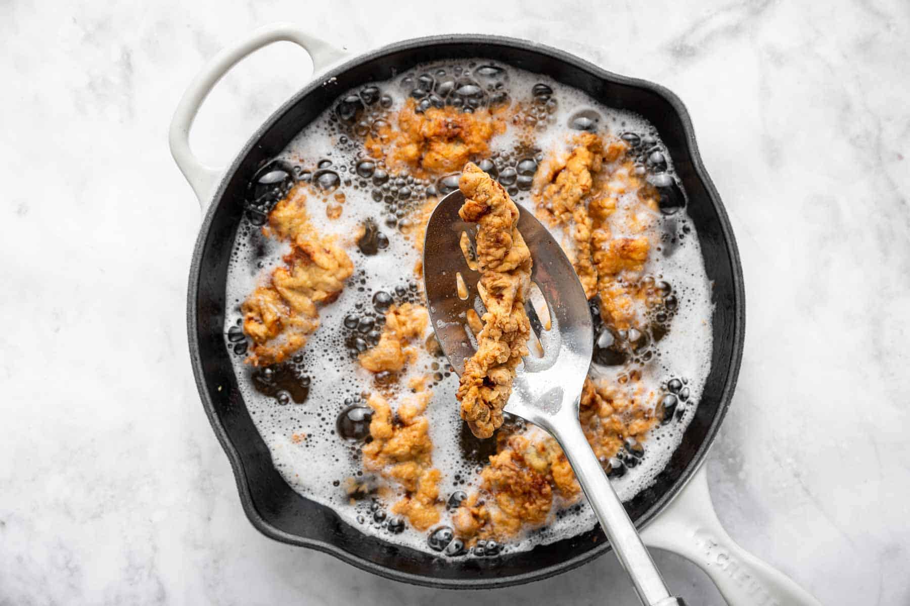 Fried meat in a slotted spoon over the pan.