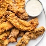 Steak fingers on a round plate with dipping sauce on side.